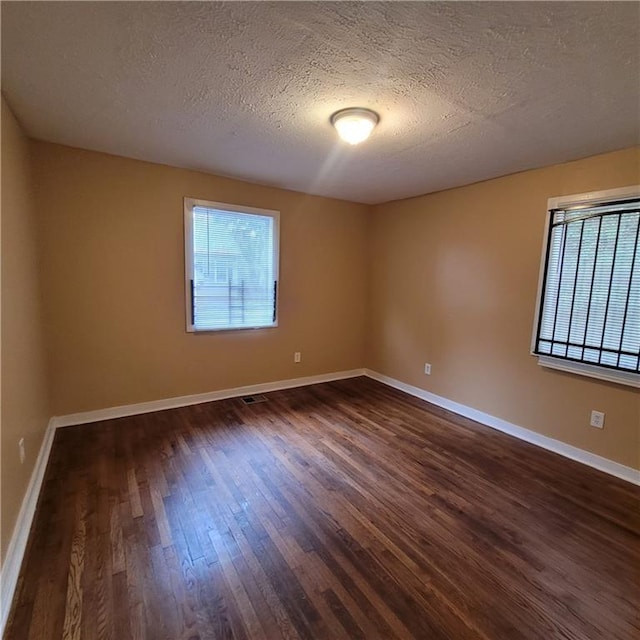 spare room with a textured ceiling, baseboards, and dark wood-style flooring