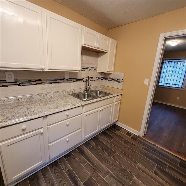 kitchen featuring baseboards, wood tiled floor, a sink, decorative backsplash, and white cabinets