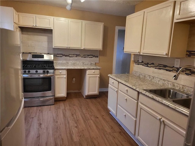 kitchen with light wood-type flooring, a sink, freestanding refrigerator, white cabinets, and gas range