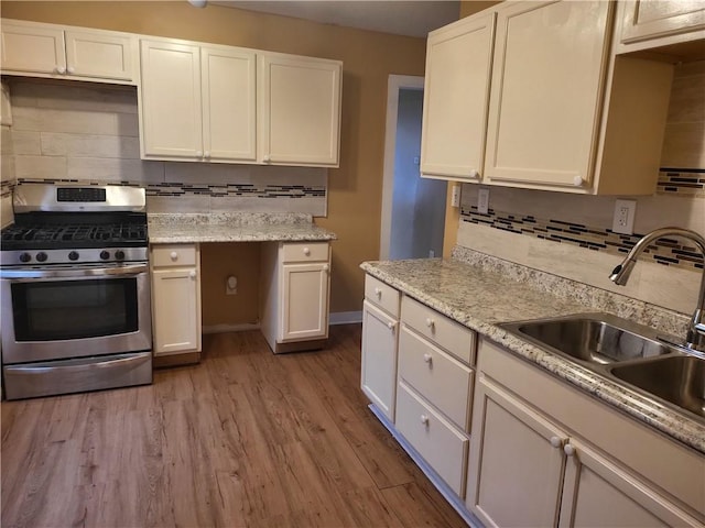 kitchen with a sink, backsplash, white cabinets, light wood finished floors, and stainless steel range with gas stovetop