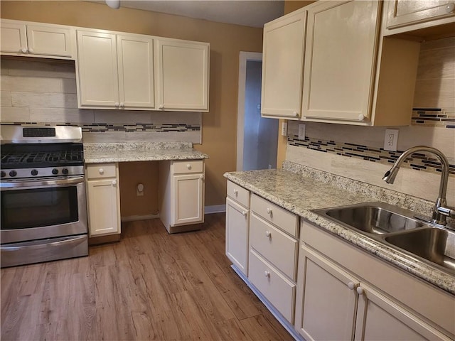 kitchen featuring stainless steel gas stove, a sink, backsplash, white cabinets, and light wood finished floors