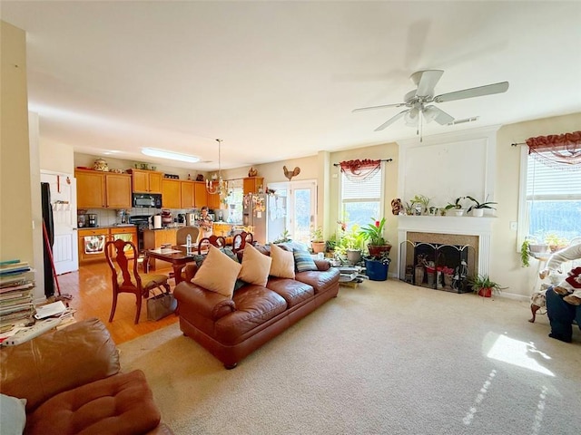 living room with ceiling fan with notable chandelier and light colored carpet