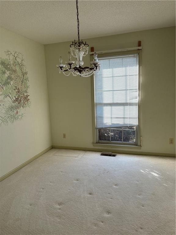 carpeted spare room featuring a textured ceiling, a wealth of natural light, and an inviting chandelier