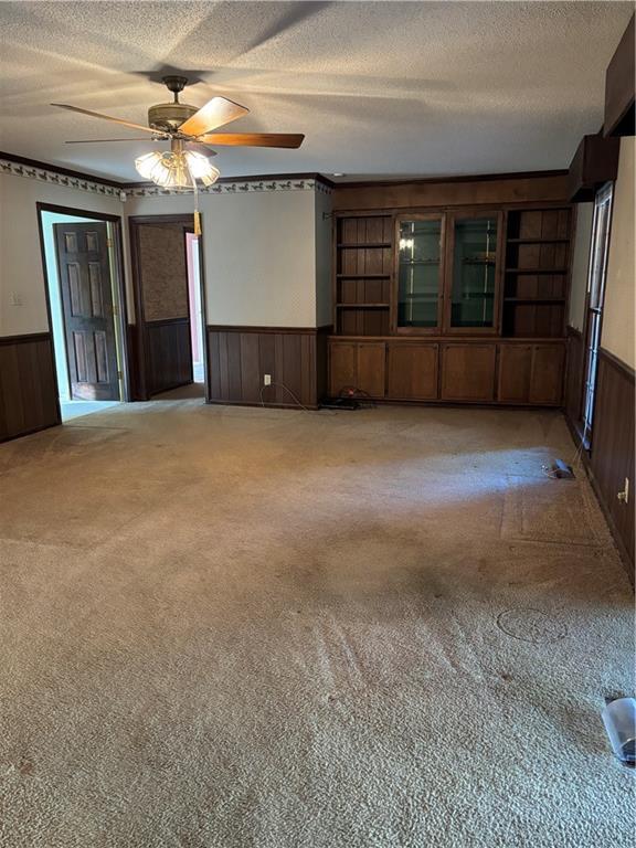 unfurnished living room with ceiling fan, wooden walls, a textured ceiling, and carpet flooring