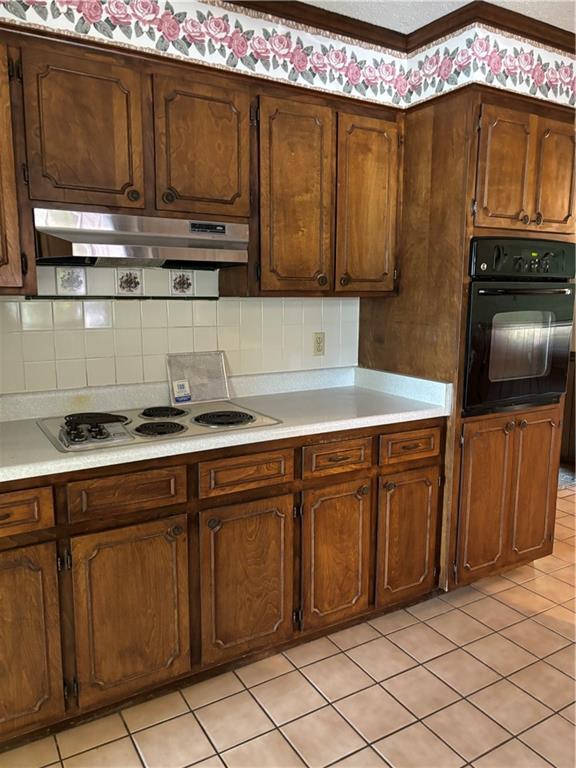 kitchen with light tile patterned floors, white cooktop, backsplash, and black oven