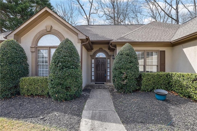 entrance to property with a shingled roof and stucco siding