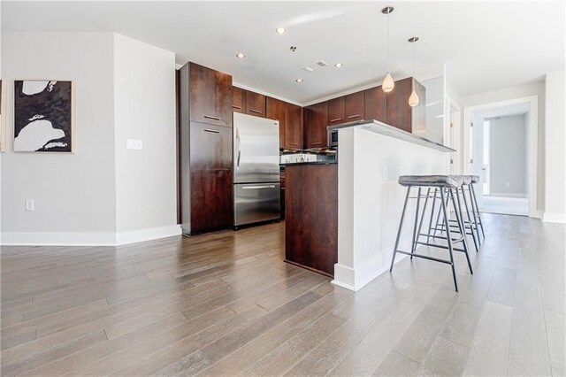 kitchen with a breakfast bar area, a center island, hanging light fixtures, light hardwood / wood-style flooring, and stainless steel fridge