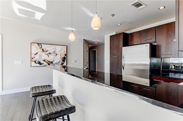 kitchen with stainless steel refrigerator, wood-type flooring, a breakfast bar area, hanging light fixtures, and kitchen peninsula