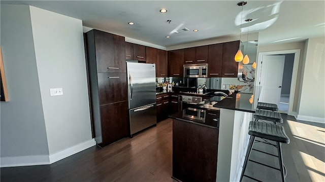 kitchen featuring appliances with stainless steel finishes, dark hardwood / wood-style floors, a kitchen breakfast bar, hanging light fixtures, and dark brown cabinets