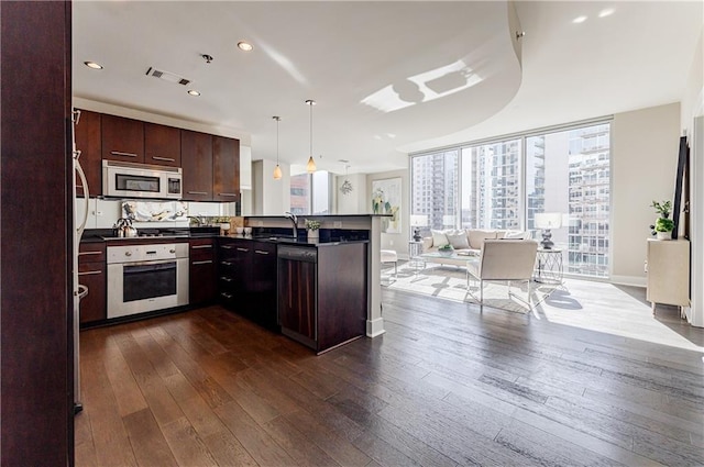 kitchen featuring decorative light fixtures, appliances with stainless steel finishes, dark wood-type flooring, and kitchen peninsula