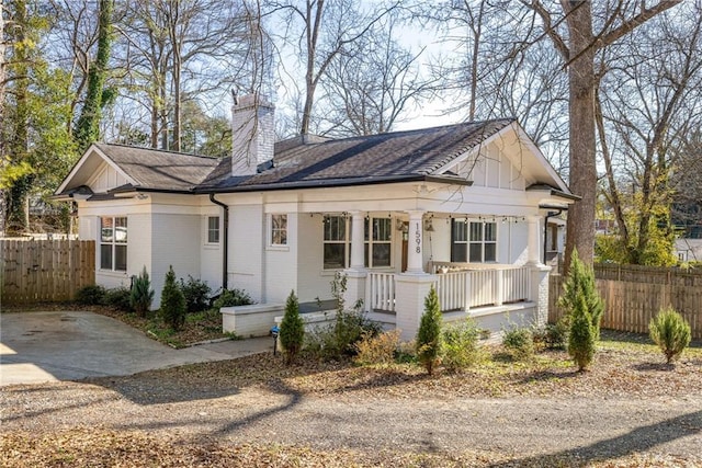 view of front facade featuring covered porch, brick siding, a shingled roof, fence, and a chimney