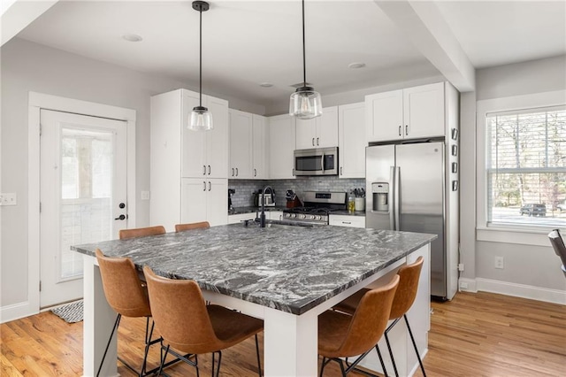 kitchen with a breakfast bar area, hanging light fixtures, appliances with stainless steel finishes, white cabinets, and an island with sink