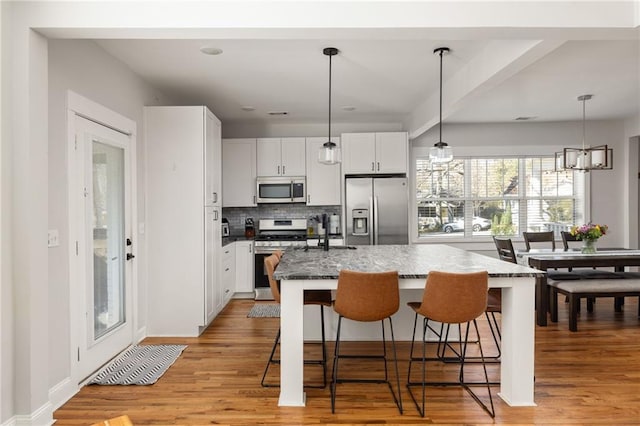 kitchen featuring a center island, a breakfast bar area, appliances with stainless steel finishes, white cabinetry, and dark stone countertops