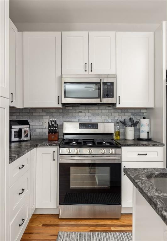 kitchen featuring dark stone counters, light wood-style flooring, stainless steel appliances, white cabinetry, and backsplash