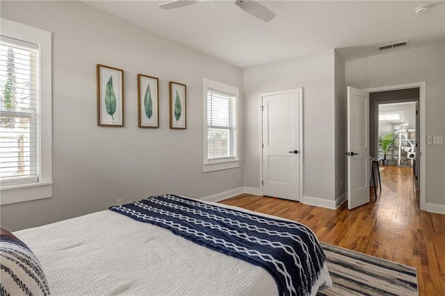 bedroom with ceiling fan, wood finished floors, visible vents, and baseboards