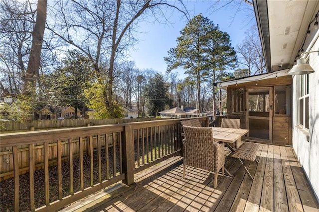 wooden terrace featuring outdoor dining space, a sunroom, and fence