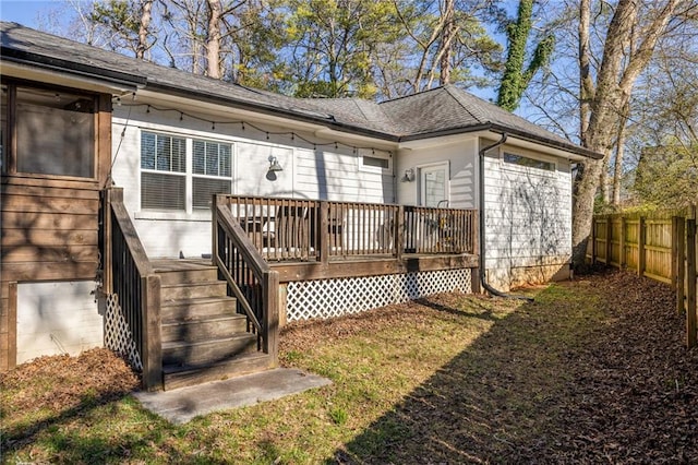 rear view of house with a shingled roof, fence, and a deck