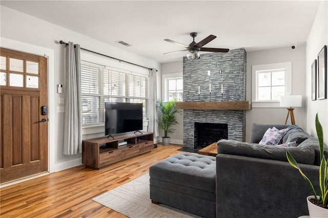 living room with a healthy amount of sunlight, visible vents, a stone fireplace, and light wood finished floors