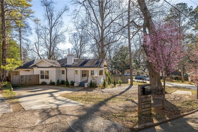 view of front of house featuring driveway, a chimney, and fence