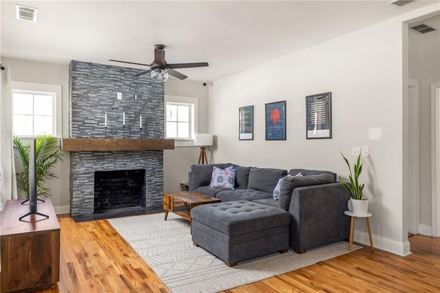 living area with visible vents, a stone fireplace, baseboards, and wood finished floors