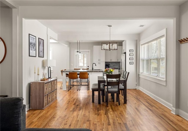 dining space with baseboards, visible vents, light wood finished floors, and an inviting chandelier