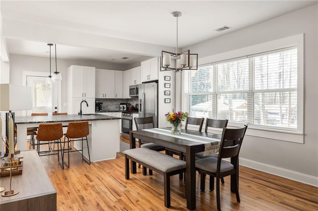 dining area with light wood finished floors, baseboards, visible vents, and a chandelier