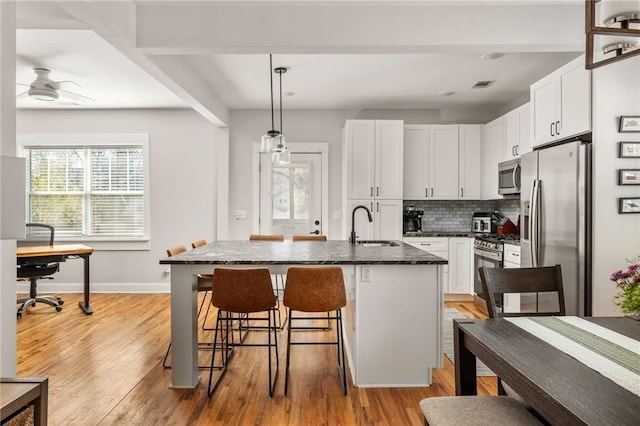 kitchen featuring white cabinets, an island with sink, decorative light fixtures, stainless steel appliances, and a sink