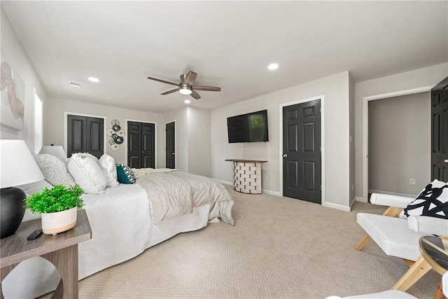 bedroom with ceiling fan, light carpet, and multiple closets