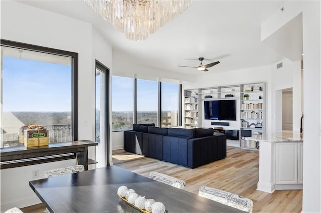 living area featuring ceiling fan with notable chandelier, visible vents, light wood-style flooring, and baseboards