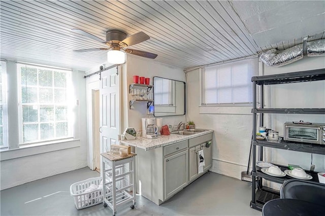 kitchen with ceiling fan, sink, wooden ceiling, a barn door, and light stone counters