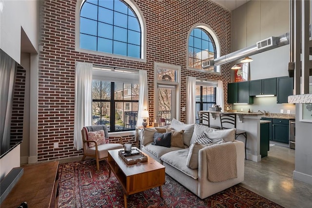 living room with visible vents, concrete floors, a towering ceiling, and brick wall