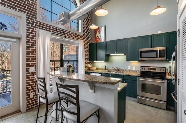 kitchen featuring stainless steel appliances, a towering ceiling, green cabinets, a sink, and brick wall