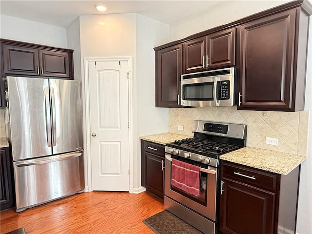 5850 Shiloh Woods Dr, Cumming, GA 30040 - kitchen featuring appliances with stainless steel finishes, dark brown cabinetry, light wood-style floors, backsplash, and light stone counters
