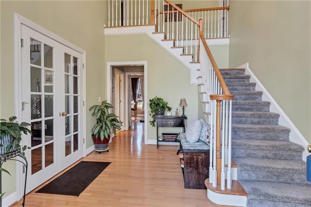 entryway featuring a high ceiling, wood finished floors, baseboards, french doors, and stairway