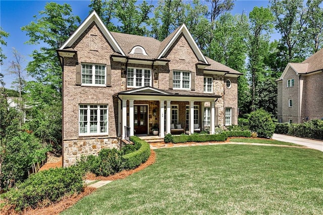 view of front facade featuring brick siding, a front lawn, stone siding, and covered porch