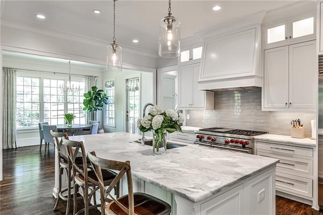 kitchen featuring custom range hood, an island with sink, range with two ovens, and white cabinetry