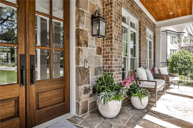 view of exterior entry with french doors, covered porch, and stone siding
