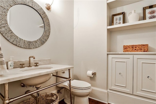 half bathroom featuring a sink, toilet, wood finished floors, and baseboards