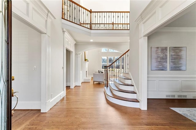 foyer with light wood finished floors, arched walkways, stairs, crown molding, and a decorative wall