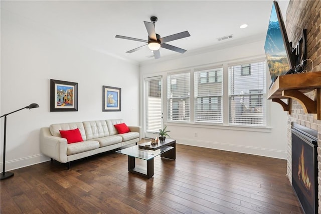 living room featuring dark wood-type flooring, ceiling fan, a fireplace, and crown molding