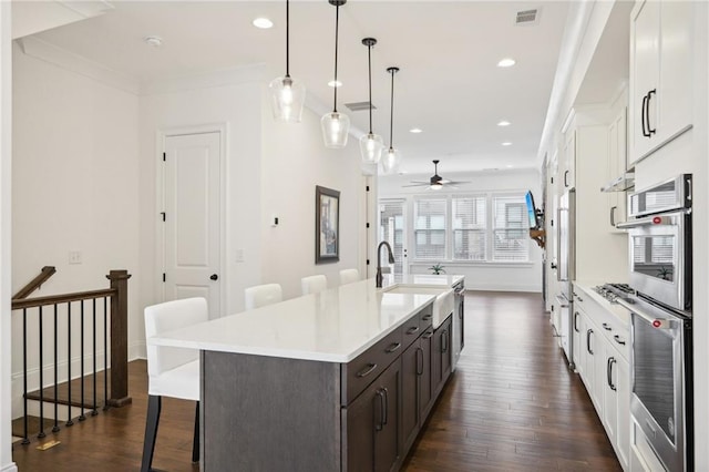 kitchen with decorative light fixtures, an island with sink, white cabinets, a kitchen breakfast bar, and ornamental molding