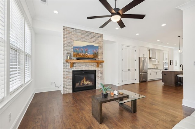 living room with crown molding, a brick fireplace, dark wood-type flooring, and a wealth of natural light