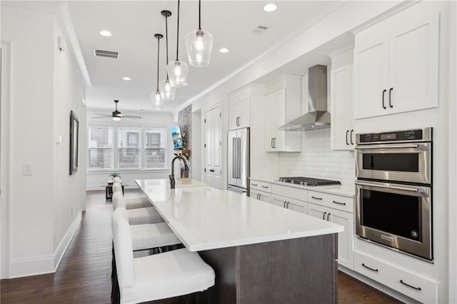 kitchen with white cabinetry, wall chimney exhaust hood, a breakfast bar, and a kitchen island with sink