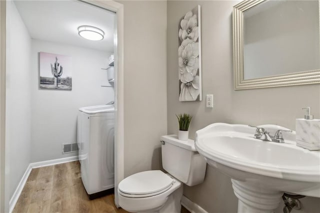 half bathroom with washer / clothes dryer, visible vents, toilet, wood finished floors, and baseboards