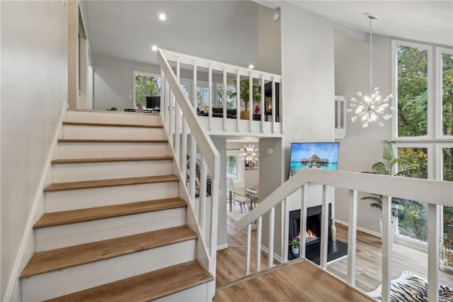 stairway with a wealth of natural light, a notable chandelier, and wood finished floors