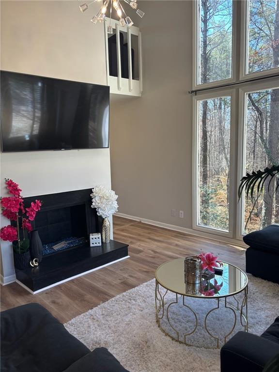 living room featuring a fireplace with raised hearth, plenty of natural light, wood finished floors, and baseboards