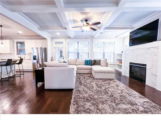 living room with ceiling fan, coffered ceiling, beamed ceiling, dark hardwood / wood-style floors, and a tiled fireplace