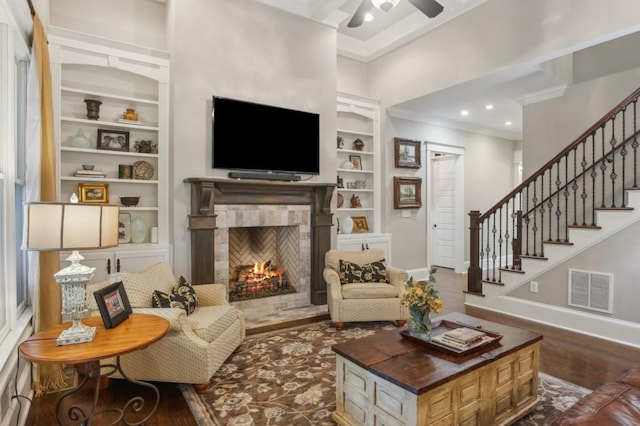 living area featuring ornamental molding, built in features, dark wood finished floors, baseboards, and a lit fireplace