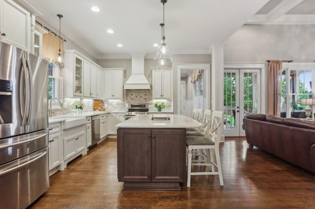 kitchen with appliances with stainless steel finishes, custom exhaust hood, crown molding, a sink, and glass insert cabinets