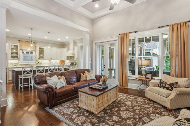 living room featuring healthy amount of natural light, dark wood-type flooring, ornate columns, a towering ceiling, and a ceiling fan